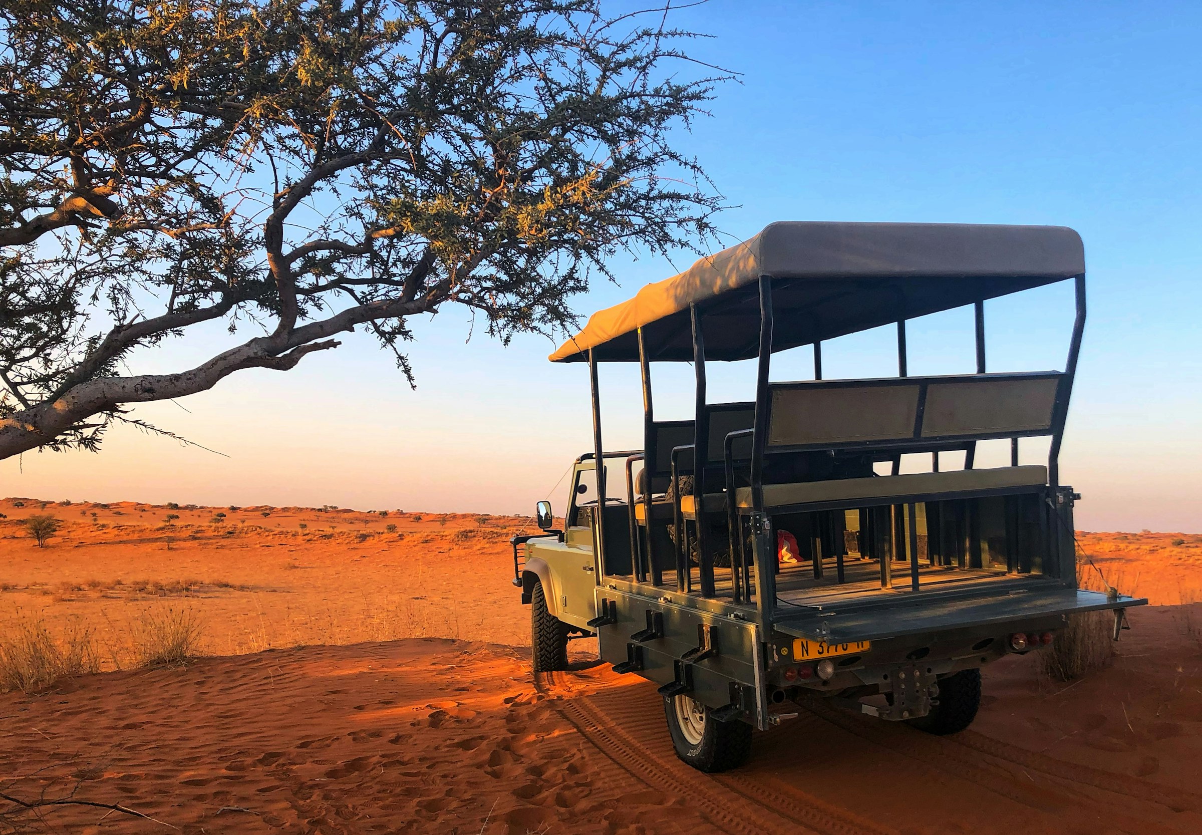 Safari jeep driving across open desert terrain at golden hour.